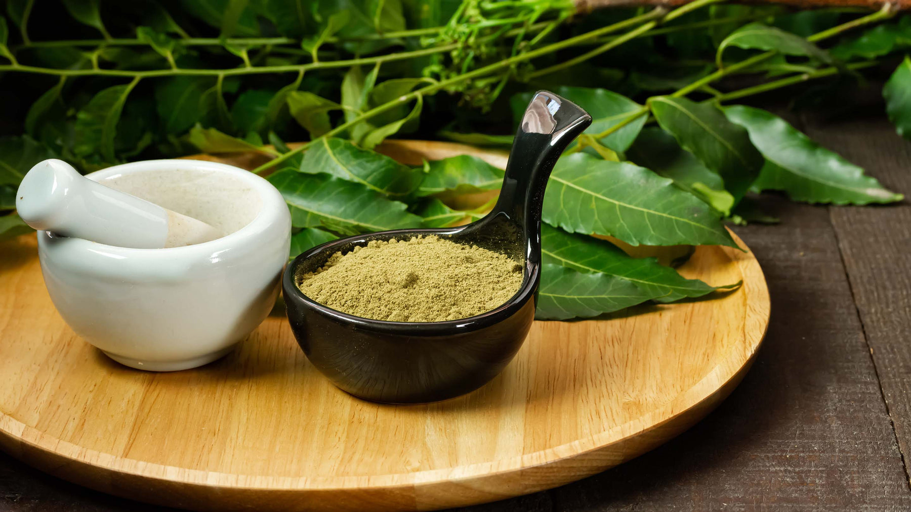 Neem powder in black bowl with neem leaf and white mortar and pestle on wooden background