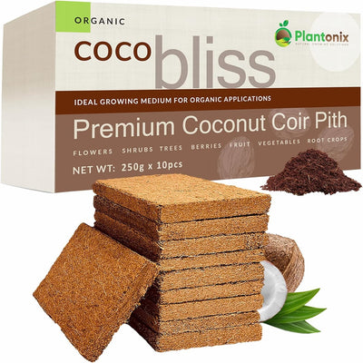 A stack of coco coir bricks in front of a box of premium coconut coir pith. There is a loose pile of hydrated coir to show texture and an open coconut. 